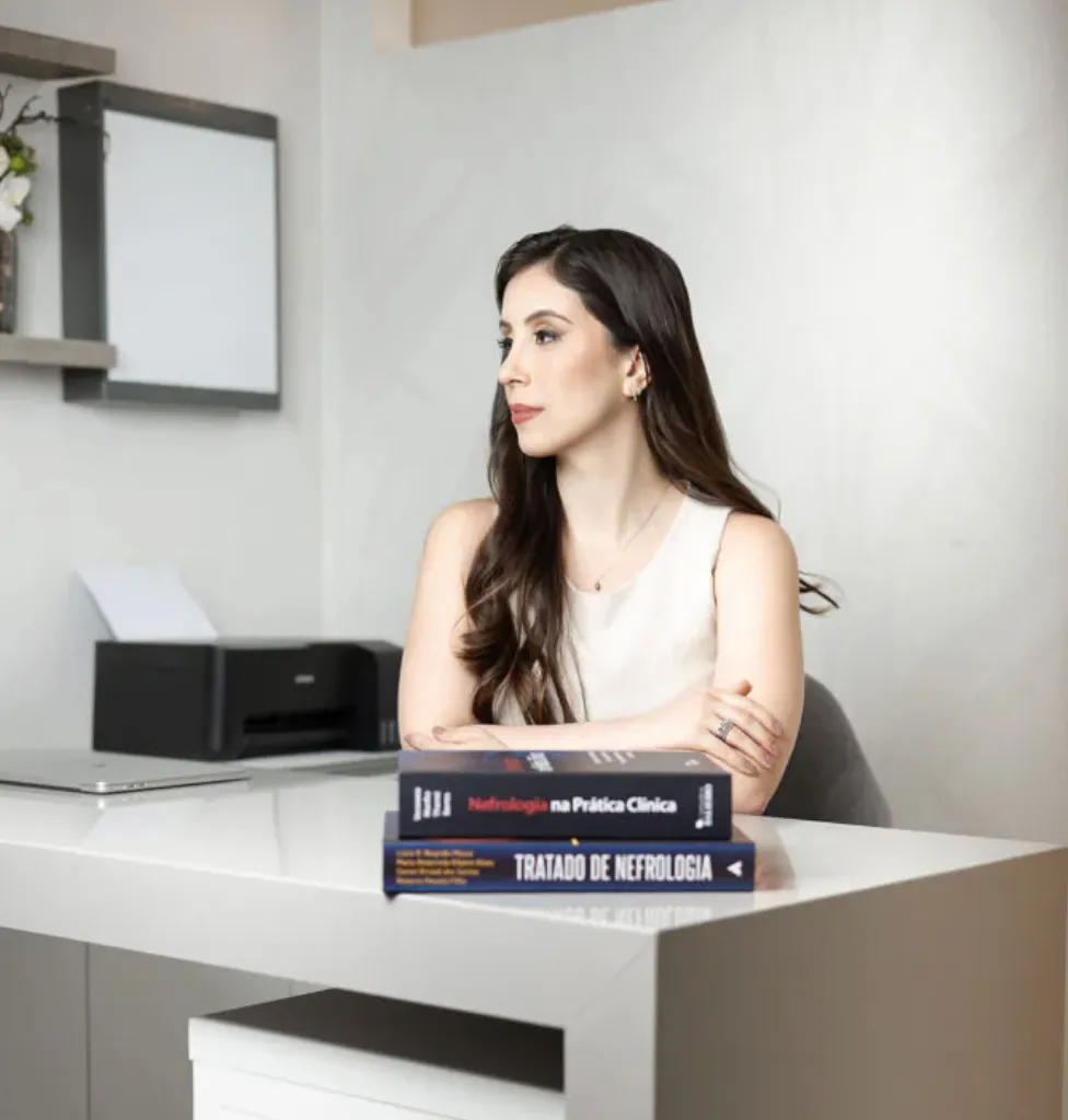 Dra. Marina Melém sentada à mesa, com livros de nefrologia